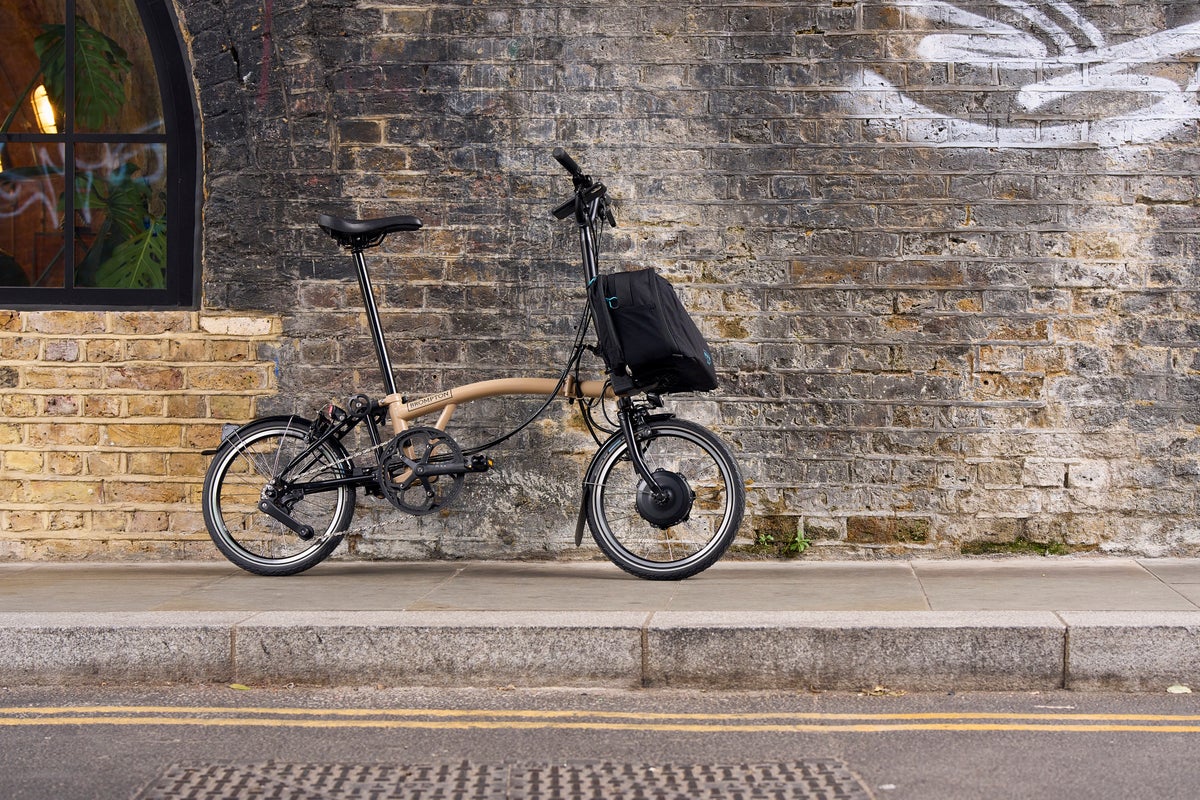 A man sitting next to a folded Brompton Electric C Line with a resting dog next to him