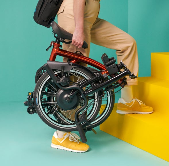 A studio shot of person carrying a folded Brompton Electric C Line 